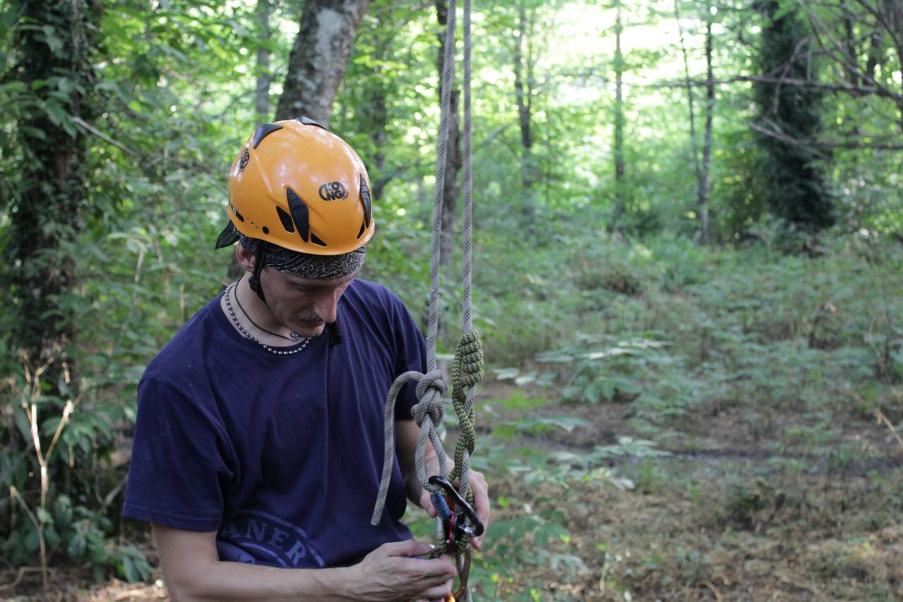 Operatore con casco che prepara nodi e moschettoni prima della salita